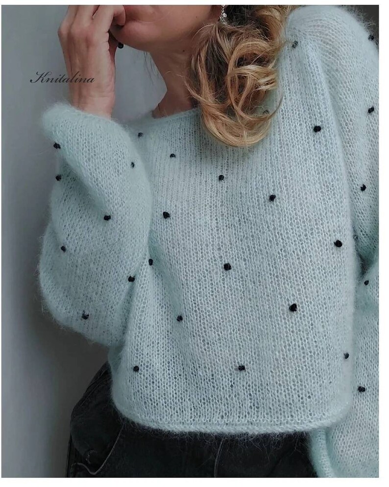 May include: A light blue knitted jumper with black beads throughout the fabric. The jumper has a loose fit and long sleeves.
