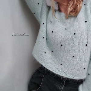 May include: A light blue sweater with black polka dots. The sweater is knitted and has a loose fit. The sweater is cropped and has a round neckline.