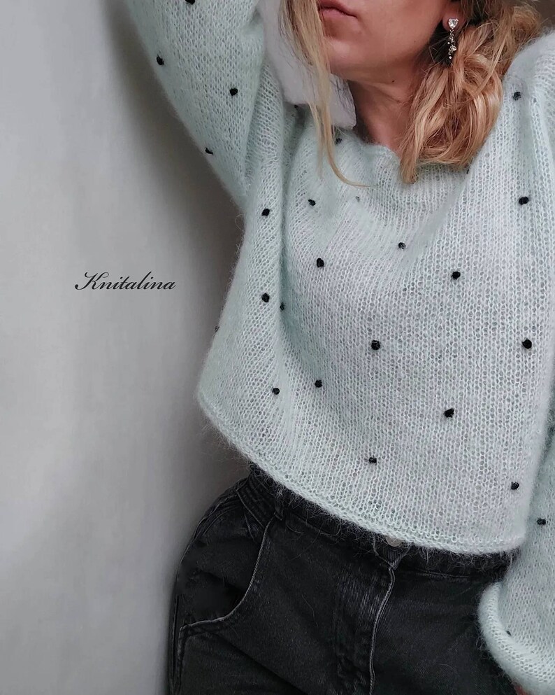 May include: A light blue sweater with black polka dots. The sweater is knitted and has a loose fit. The sweater is cropped and has a round neckline.
