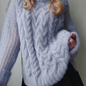 Peut inclure: Un pull en maille douce bleu clair avec un motif en tricot torsad&eacute;. Le pull a un col rond et des manches longues.