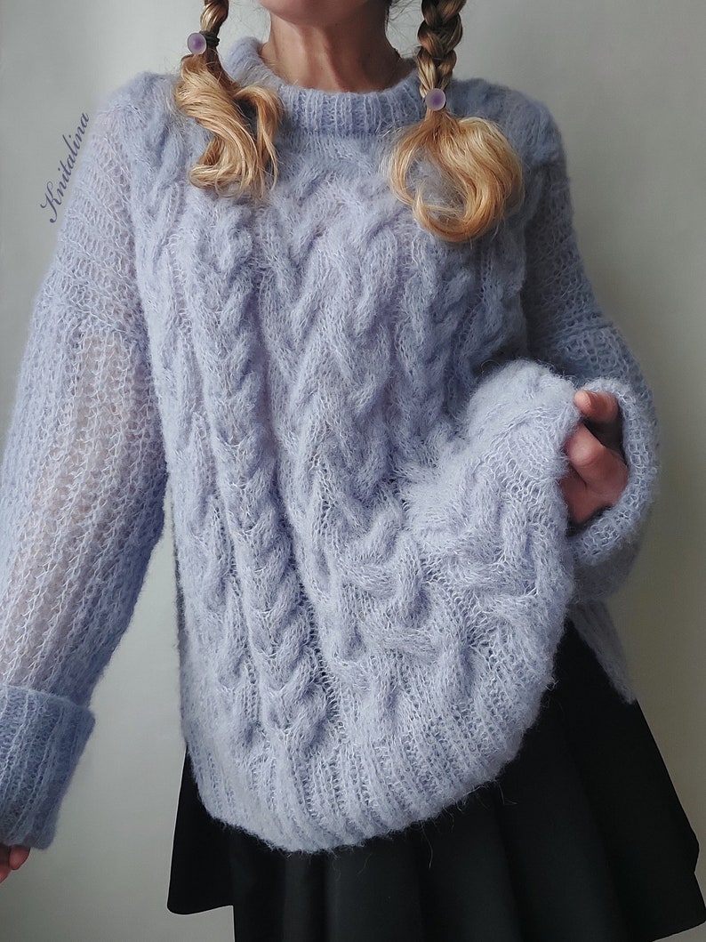 Peut inclure: Un pull en maille douce bleu clair avec un motif en tricot torsad&eacute;. Le pull a un col rond et des manches longues.