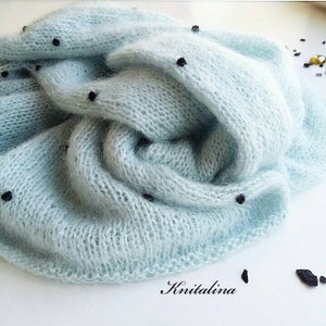 May include: A light blue knitted scarf with black dots. The scarf is made of a soft, fuzzy material and is folded in a loose, casual way.