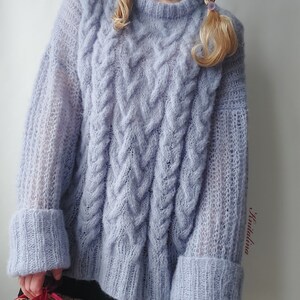 Peut inclure: Un pull en maille torsad&eacute;e surdimensionn&eacute; bleu clair &agrave; manches longues et &agrave; la coupe ample. Le pull a un aspect textur&eacute; et duveteux et pr&eacute;sente un motif en maille torsad&eacute;e.