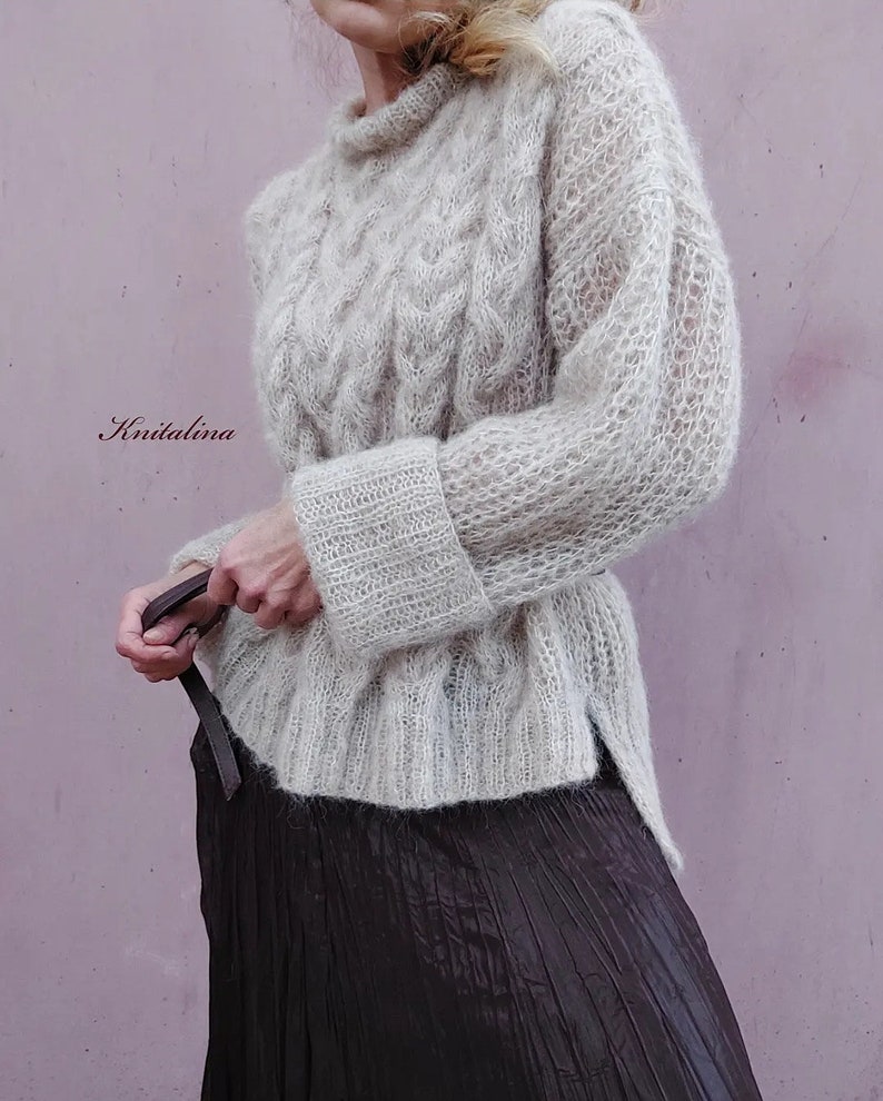 Peut inclure: Un pull en maille beige clair avec un motif en tricot torsad&eacute; et des manches longues. Le pull a une coupe ample et une longueur l&eacute;g&egrave;rement plus longue dans le dos.