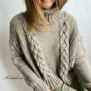 May include: A beige knitted jumper with a high neck and cable knit detail. The jumper has a relaxed fit and is made of a soft, comfortable material.