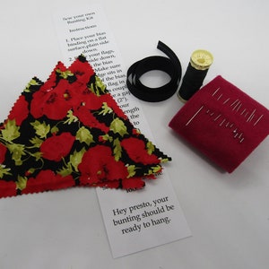 Può includere: Un kit per la creazione di bandierine con istruzioni, tessuto rosso con stampa di papaveri, nastro di sbieco nero, filo nero, un rocchetto di filo e un cuscino per spilli con spilli.