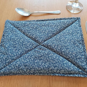 Può includere: Un tovaglietta da tavola in tessuto blu e bianco con motivo floreale e design trapuntato. La tovaglietta è piegata a metà e ha un bordo bianco.
