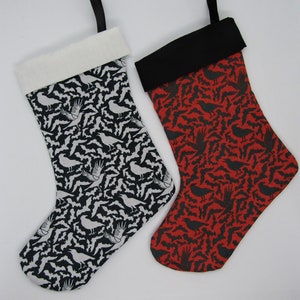 Puede incluir: Dos calcetines de Navidad, uno blanco y negro con un patrón de pájaros y otro rojo con un patrón de pájaros negros.