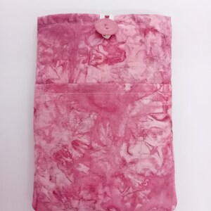 Può includere: Una pochette in tessuto rosa con chiusura a bottone bianco. Il tessuto ha un motivo tie-dye in tonalità di rosa e bianco.