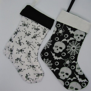 Puede incluir: Dos calcetines de Halloween, uno con un patrón de esqueleto blanco y negro y el otro con un patrón de calavera, araña y murciélago blanco y negro.