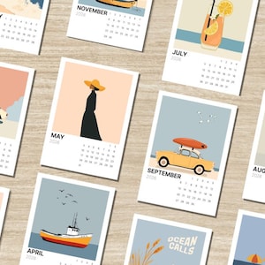 Könnte beinhalten: Eine Sammlung illustrierter Kalender für 2026 mit Strandmotiven. Jeder Kalender zeigt einen anderen Monat mit Bildern von Autos, Booten, Personen und Cocktails. Die Kalender sind auf einer hellbraunen Holzoberfläche angeordnet.