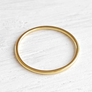 Könnte beinhalten: Ein einfacher, goldfarbener Ring. Der Ring ist ein dünnes, kreisförmiges Band, das auf einer weißen Oberfläche liegt. Der Ring ist wahrscheinlich aus Metall und hat eine glatte, polierte Oberfläche. Ein minimalistisches Schmuckstück.