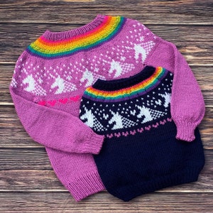 Peut inclure: Deux pulls en tricot avec un motif arc-en-ciel et des motifs de licorne. Le plus grand pull est rose et le plus petit est bleu marine.