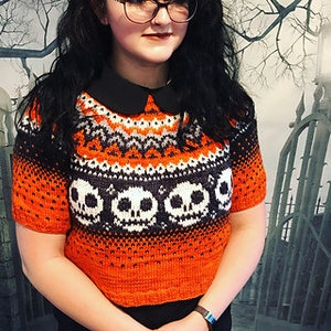 May include: Orange and black short-sleeved sweater with a skull pattern and a white collar.