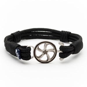 Könnte beinhalten: Schwarzes geflochtenes Armband aus Seil mit einem silbernen Anker und einem silbernen Rad-Anhänger.