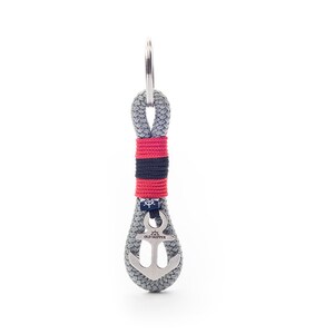 May include: A gray rope keychain with a red, black, and white striped band and a silver anchor charm with the text "Old Skipper".