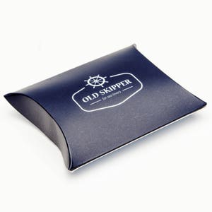 May include: A dark blue pillow-shaped box with a white logo that says "OLD SKIPPER - for sea lovers" and a white image of a ship's wheel.