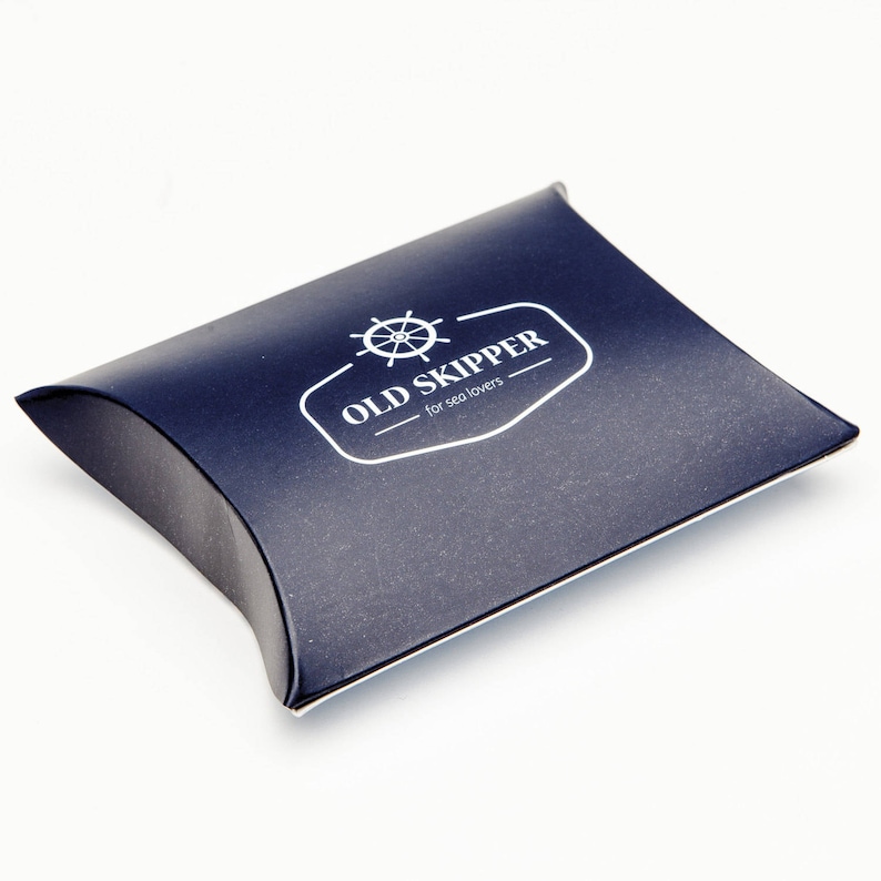 May include: A dark blue pillow-shaped box with a white logo that says "OLD SKIPPER - for sea lovers" and a white image of a ship's wheel.