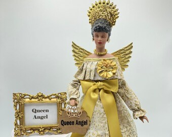 May include: A gold angel doll with a crown, wings, and a yellow dress. The doll is holding a sign that says "Queen Angel".