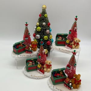 May include: Four miniature Christmas tree centerpieces with red and green toy chests, teddy bears, and the words "Merry Christmas".