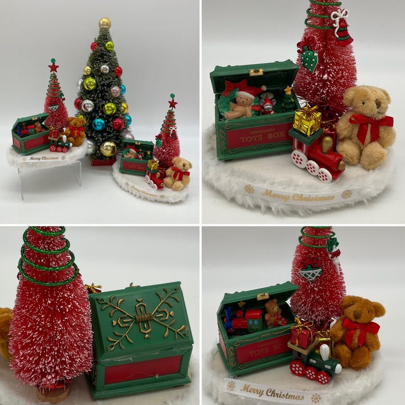 May include: A Christmas-themed toy box with a red and green design. The box is open and filled with toys, including a teddy bear, a train, and a small Christmas tree. The box is surrounded by a white fluffy base and a white ribbon with the text "Merry Christmas".