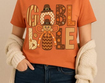 Könnte beinhalten: Orangefarbenes T-Shirt mit dem Text "GOBBLE LOVE" in einem herbstlichen Design. Die Buchstaben sind mit Mustern, Kürbissen und einer Truthahnfigur verziert. Das Shirt hat einen Rundhalsausschnitt und kurze Ärmel.