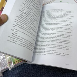 May include: An open book titled The Apothecary Diaries with white pages featuring black printed text. The left page shows dialogue and narrative paragraphs, while the right page continues the story with page number 178 visible at the bottom right corner.