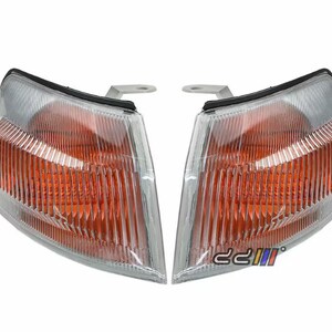 Puede incluir: Un par de luces de señal de giro de coche transparentes de color ámbar con un soporte de montaje plateado. Las luces tienen un diseño acanalado y están diseñadas para un vehículo.