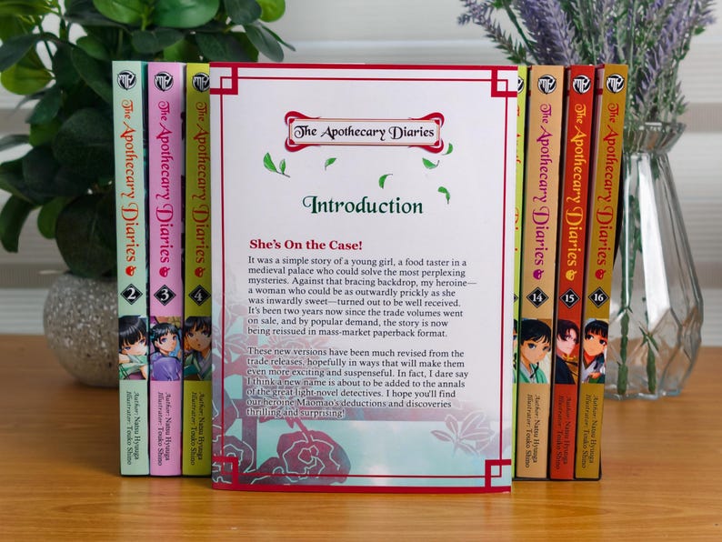 May include: A collection of The Apothecary Diaries paperback books arranged in a row. The central book is open to an introduction page titled She's On the Case! with red border accents. The spines show various volume numbers and character art.