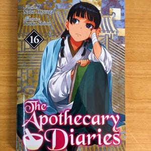 May include: The Apothecary Diaries volume 16 manga book featuring an illustration of a character with dark hair in a blue and white robe holding a green book. The cover includes the text Author: Natsu Hyuuga, Illustrator: Touko Shino, and 16.