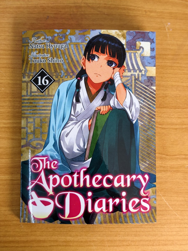May include: The Apothecary Diaries volume 16 manga book featuring an illustration of a character with dark hair in a blue and white robe holding a green book. The cover includes the text Author: Natsu Hyuuga, Illustrator: Touko Shino, and 16.