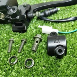Op de afbeelding: Zwarte motorfiets remhendel assemblage met een hoofdcilinder, een hendel, een kabel en een zwarte klem. De assemblage bevindt zich op een groene ondergrond met vier zilveren schroeven en twee zilveren ringen.