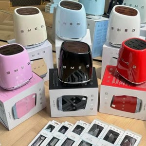 May include: A collection of SMEG knife blocks in various colors, including pink, black, red, white, and blue. Each block has a stainless steel base and a wooden knife insert. The SMEG logo is visible on the front of each block.