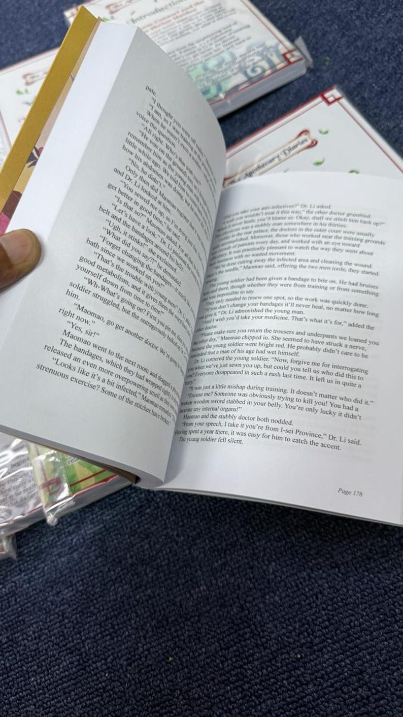 May include: An open book titled The Apothecary Diaries with white pages and black printed text. The left page shows dialogue between characters, while the right page features a header with the title and continues the narrative text.