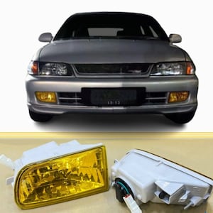 May include: A pair of yellow fog lights for a car. The lights are made of clear plastic with a yellow lens. The lights have a white plastic housing and a black wire connector.