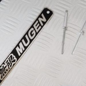 May include: A silver metal plate with the word "MUGEN" in black lettering and Japanese characters. Two silver metal rivets are included.