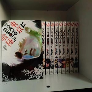 May include: A collection of manga volumes, including "Tokyo Ghoul" volume 14, displayed on a shelf. The spines of the books are visible, with the title "Tokyo Ghoul" printed vertically. The covers feature character illustrations.