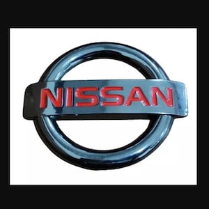 May include: A silver car emblem with a red "NISSAN" logo in the center.