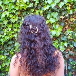 May include: A person with long, curly brown hair wearing a pink strapless dress. They have a gold crescent moon and star hair clip in their hair.