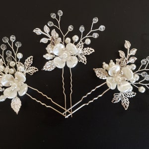May include: Three silver hair pins with white pearl flowers and crystal accents. The flowers have a delicate, feminine design.