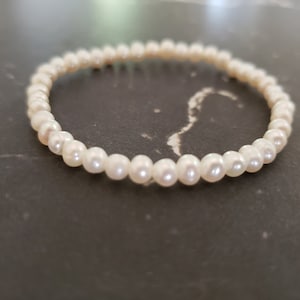 May include: A white pearl bracelet with a simple design. The bracelet is made of small, round pearls that are strung together on a thin string.