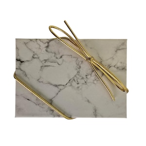 May include: A rectangular gift box with a marble pattern, tied with a gold-colored cord. The cord is looped into a bow on top of the box. The box is white with gray veining.