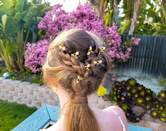 May include: A set of small bee-shaped hair pins featuring yellow and black striped bodies with clear crystal wings. The pins are secured into a braided hairstyle, with each bee ornament positioned along the length of the braid to add detail.