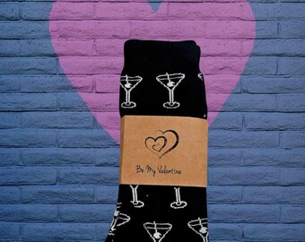 May include: Black socks with a white martini glass pattern. The socks are packaged in a brown box with a white heart and the text "Be My Valentine".