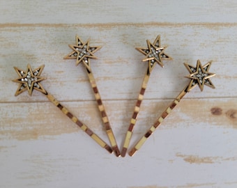 May include: Four gold hair clips with a star-shaped design. Each star is adorned with clear rhinestones.
