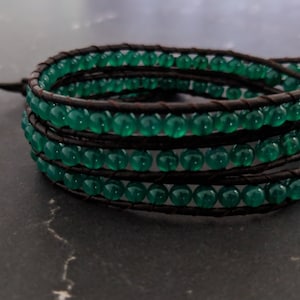 May include: A green gemstone bracelet with brown leather wrappings. The bracelet is made of multiple strands of green beads and brown leather cord.