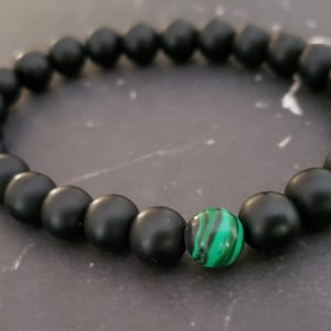 May include: A black beaded bracelet with a single green and black malachite bead.