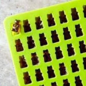 May include: Green silicone mould with 36 bear-shaped cavities. The mould is filled with a clear, amber-coloured substance, resembling gummy bears.