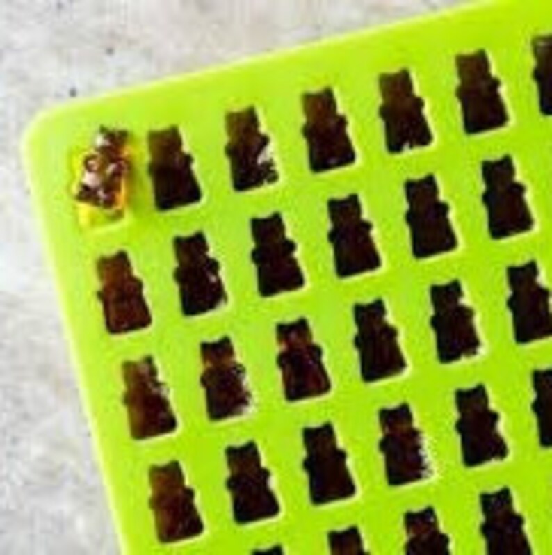 May include: Green silicone mould with 36 bear-shaped cavities. The mould is filled with a clear, amber-coloured substance, resembling gummy bears.