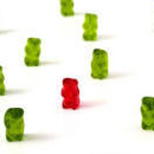 May include: A single red gummy bear surrounded by a group of green gummy bears.